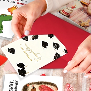 Detail of graduation greeting card being placed into a red envelope with festive decor