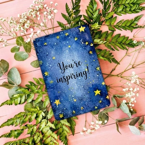 Flat lay of starry sky card with 'You're inspiring!' text and green leaf decoration