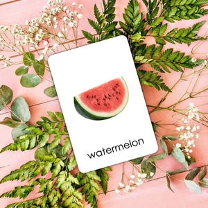 Detalle de tarjeta educativa de sandía con fruta realista sobre fondo rosa de madera