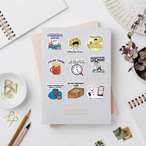 Close-up of humorous cartoon meme stickers on a grid notebook with stationery decor