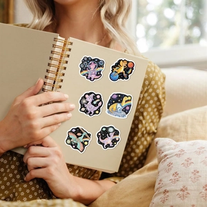Cartoon space dinosaur stickers applied on a notebook cover held by a female hand