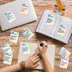 Flat lay of daily affirmation cards with watercolor gradient on a wooden desk with laptop