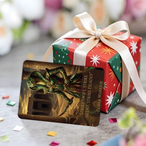 Detail einer Fantasy-Kobrakriegerkarte neben einer weihnachtlichen Geschenkbox mit Schneeflocken