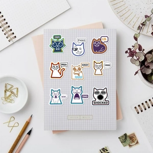 Flachbild von neun Cartoon-Katzen-Emoji-Stickern auf einem Notizbuch mit Schreibtischzubehör
