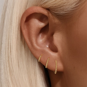Macro shot of three gold beaded s925 silver hoop earrings worn on the earlobe and cartilage