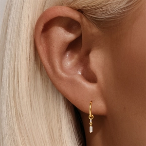 Close-up of gold geometric earring featuring a rectangular clear zircon stone on model