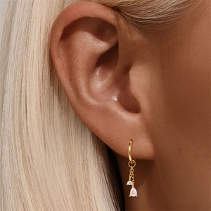 Detail of gold drop earrings with dangling zircons worn by a model in a close-up shot