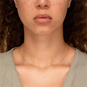 Minimalist gold necklace with three sparkling small diamonds worn on neck closeup