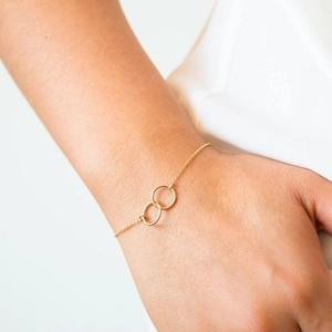 Nahaufnahme eines minimalistischen goldenen Armbands mit zwei ineinandergreifenden Ringen