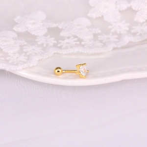 Detail of star-shaped gold stud earring with clear zircon on a white ceramic dish