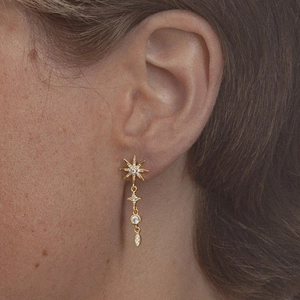 Close-up of a gold-plated sterling silver earring with star and teardrop charms on a model