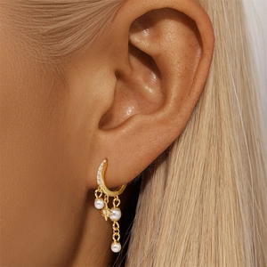 Close-up of a gold star earring with pearls and diamonds worn on an earlobe