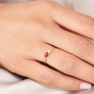 Nahaufnahme eines birnenförmigen Rubinrings mit Diamanten in Roségold am Finger