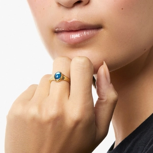Detailansicht eines vergoldeten Rings mit ovalem blauem Edelstein an der Hand