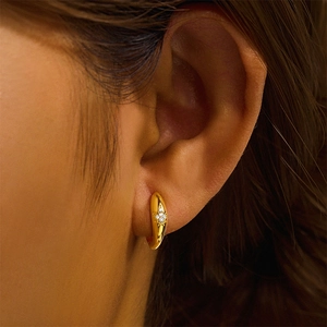 Close-up of golden curved hoop earring with four white zircon stones on a model's ear