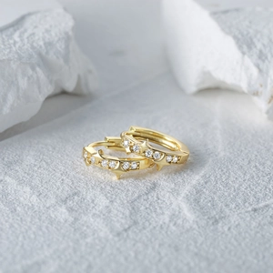 Detail of gold hoop earrings with white zircons and star accents on stone base