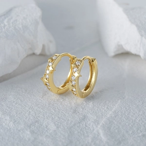 Detailed view of gold star-patterned huggie earrings with cubic zirconia stones on stone