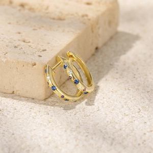 Close-up of gold hoop earrings with colorful inlaid crystals on textured stone
