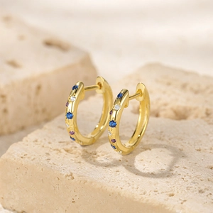 Macro detail of gold huggie earrings featuring inlaid blue and purple cubic zirconia stones