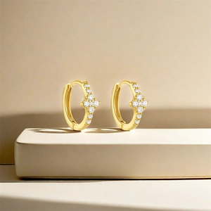 Detail of gold-plated hoop earrings featuring zircon-encrusted star charms on a beige stand
