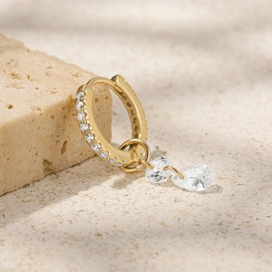 Detalle de pendientes de aro dorados con circonitas blancas y colgantes de gota