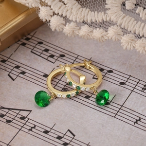 Foto macro de pendientes de aro dorados con esmeralda y circonitas sobre partitura