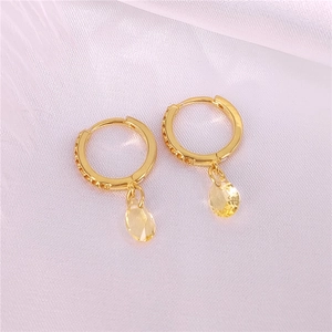 Detalle de pendientes de aro dorados con colgantes de cristal amarillo brillante