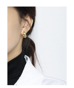 Detailed close-up of a polished gold teardrop earring on a model's earlobe