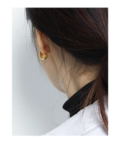 Close-up of minimalist chunky golden oval earring worn by a model in soft lighting