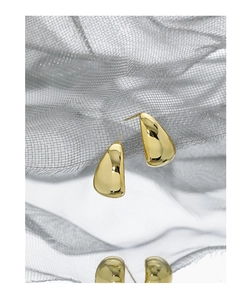 Macro shot of minimalist teardrop gold earrings with a polished mirror finish on fabric