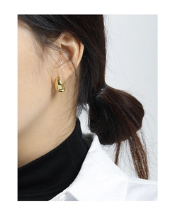 Close-up of minimalist gold teardrop stud earrings with polished mirror finish on a model