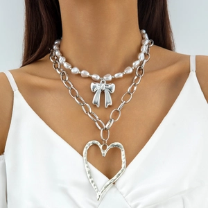 Close-up of layered necklace featuring faux pearls, bow charm, and large hammered heart pendant