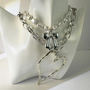 Detail of layered necklace featuring faux pearls, silver bow, and textured heart pendant