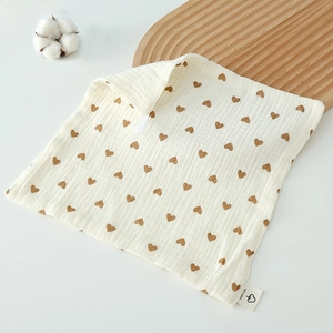 Detail of white cotton baby washcloth with brown heart pattern on a wooden tray