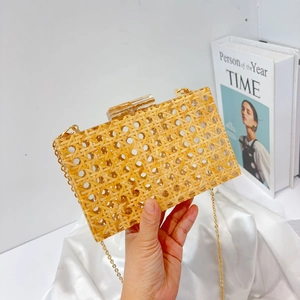 Close-up of a woven rattan acrylic clutch bag with a gold chain and metal lock clasp