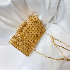 Detail of woven straw clutch with acrylic clasp and gold metal chain strap on silk