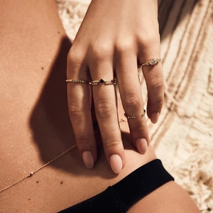 Detail of minimalist gold-plated rings with black zircon stones and a delicate body chain
