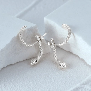 Macro shot of silver snake stud earrings with textured scales and black stone eyes