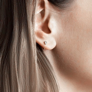 Macro side view of minimalist silver snake stud earring worn on a female earlobe