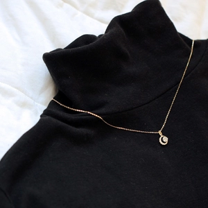 Détail d'un collier croissant de lune plaqué or porté sur un col roulé noir élégant