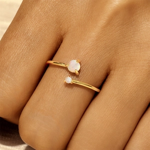 Detailed view of adjustable gold ring with two round white opal stones on model's finger
