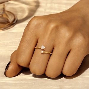 Close-up of minimalist adjustable gold ring with two round opals worn on a finger