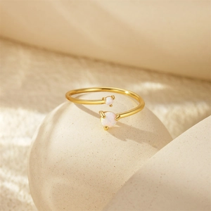 Detailed close-up of a gold open ring featuring two white opals on a textured surface