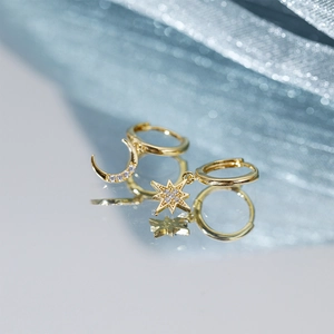 Macro view of gold asymmetric star and moon drop earrings with clear stones and ring clasps