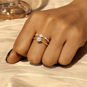 Detail of a thin gold band ring with a round white pearl and zircon accents on silk