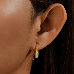 Close-up of a gold teardrop earring with micro-inlaid diamonds in a minimalist luxury style