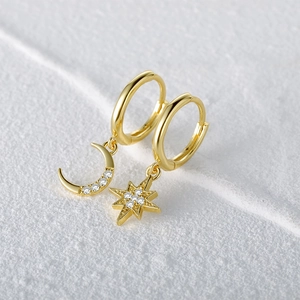Macro detail of gold asymmetric earrings featuring star and moon charms with cubic zirconia