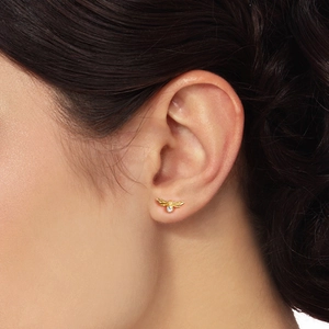 Close-up of a tiny golden bee stud earring with a sparkling zircon on a woman's earlobe