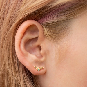 Close-up of a golden bee stud earring featuring a vibrant green gemstone on a model's ear
