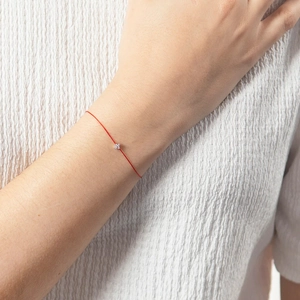 Close-up of minimalist S925 silver four-leaf flower charm on delicate red string bracelet